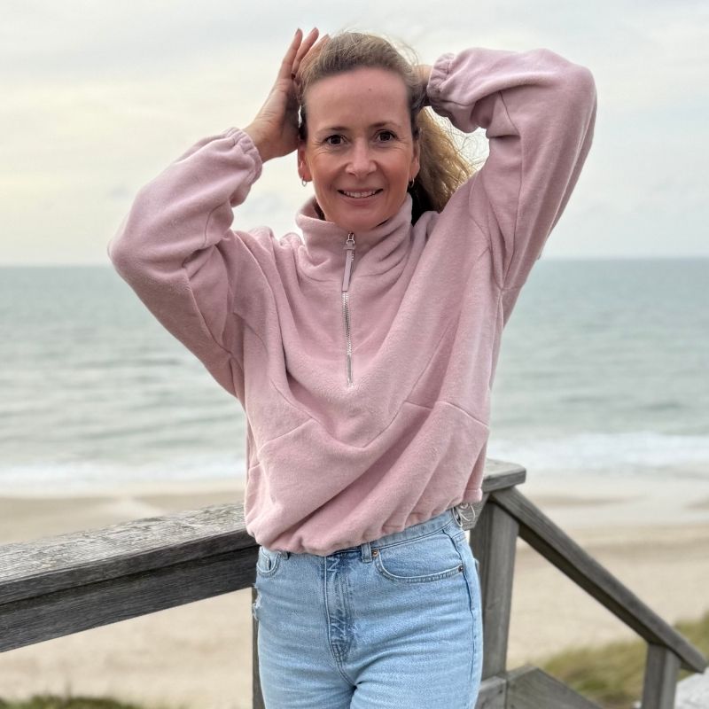 Frau trägt rosa Fleecepulli aus Bio-Baumwolle beim Strandspaziergang