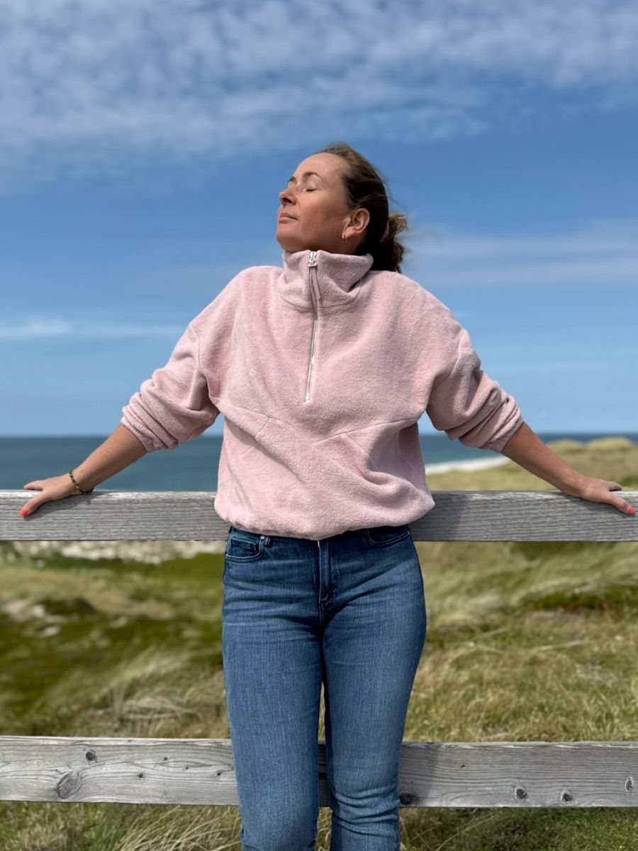 Frau trägt rosa Fleecepulli aus Bio-Baumwolle beim Spaziergang auf Sylt