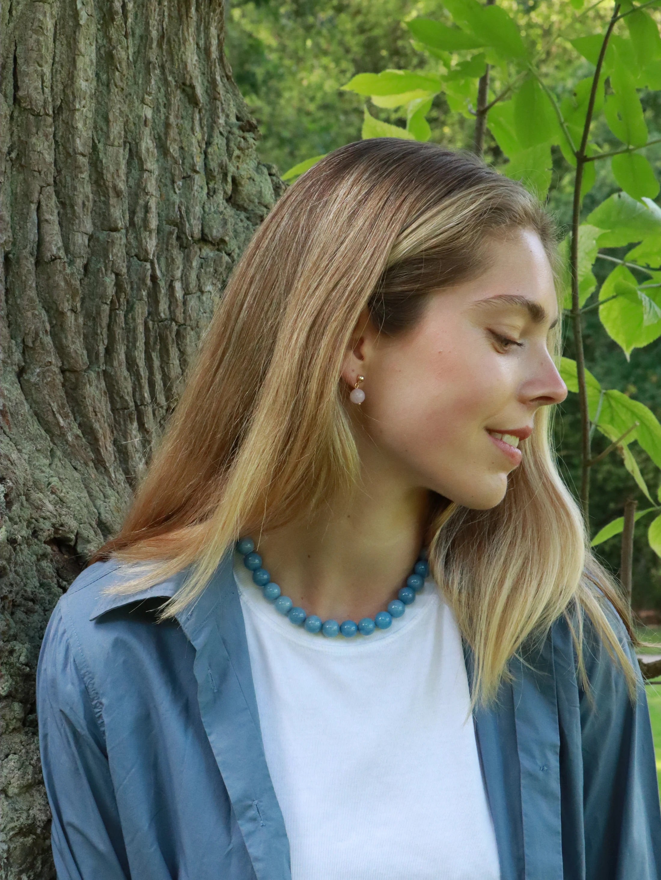 blonde Frau mit weißem shirt trägt Perlenkette aus aquamarin und ohrringe aus rosa jade