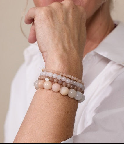 Frau trägt weißes Hemd mit 4 Perlenarmbändern aus rosa Jade, Mondstein und Sonnenstein am Handgelenk.