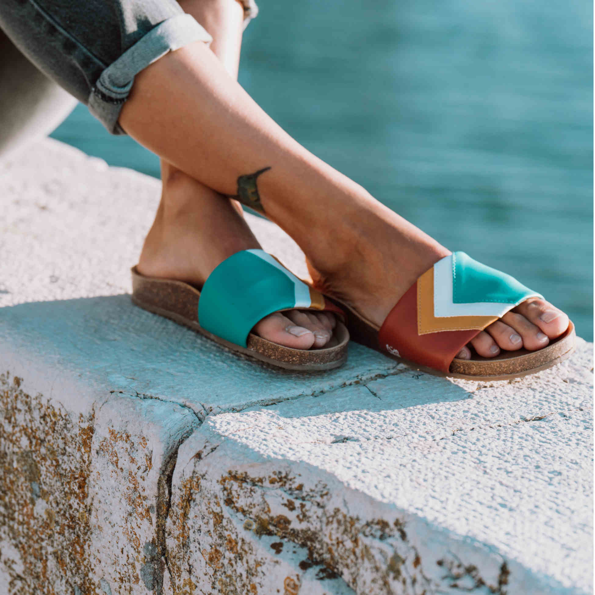 Mit PETA Vegan Award 2023 ausgezeichnete türkis-braune Sandalen; vegan mit Fußbett; Farben Ocean, Weiß, Senf, Terracotta; Marke Fünve; Modell Sunset; Mood auf Mauer