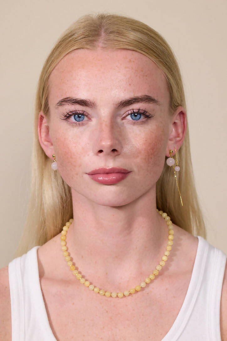 Frau trägt Perlenkette aus gelber jade und Ohrringe aus rosa Jade