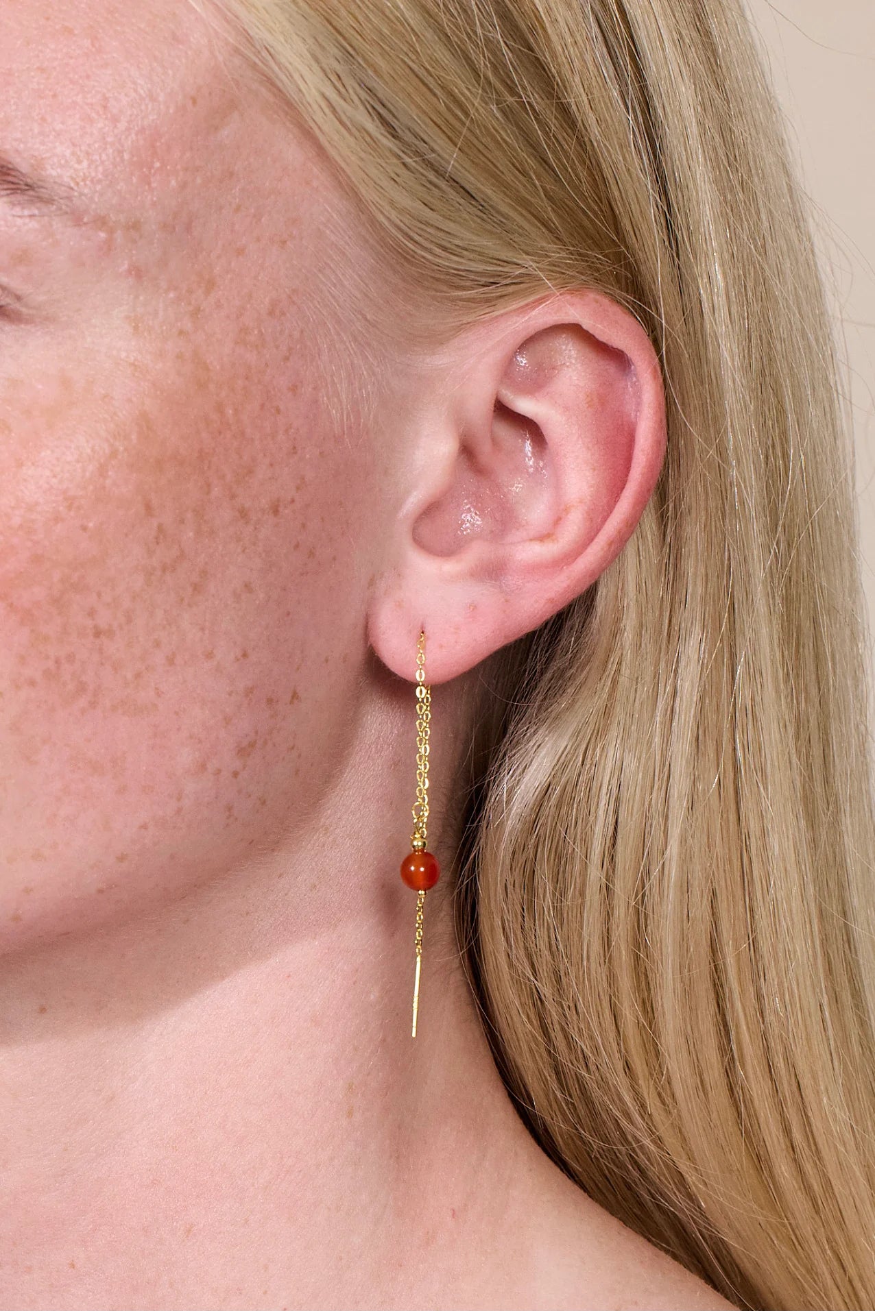 Goldener Ohrring mit roter Jadeperle getragen von einer blonden Frau